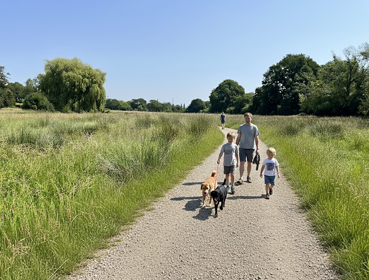 Image of young family with dogs walking along a path in green open space
